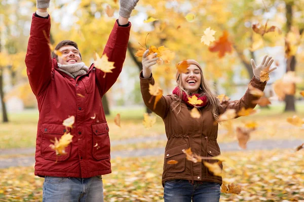 Счастливая молодая пара бросает осенние листья в парке — стоковое фото