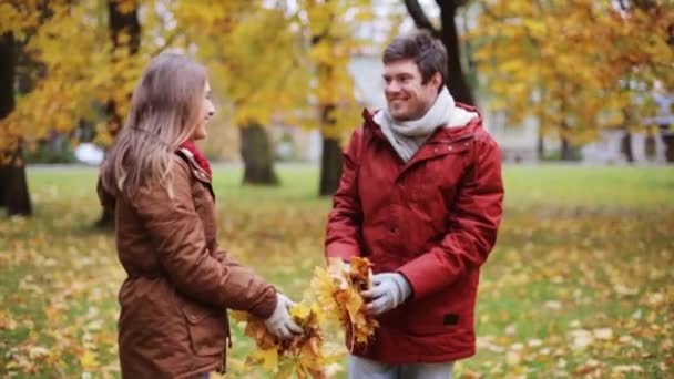 Gelukkige jonge paar gooien herfst bladeren in park — Stockvideo