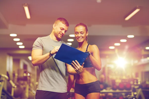 Lächelnde junge Frau mit Personal Trainer im Fitnessstudio — Stockfoto