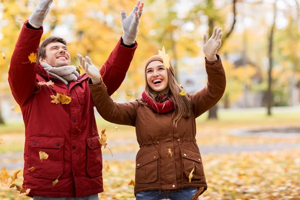 Heureux jeune couple jetant des feuilles d'automne dans le parc — Photo