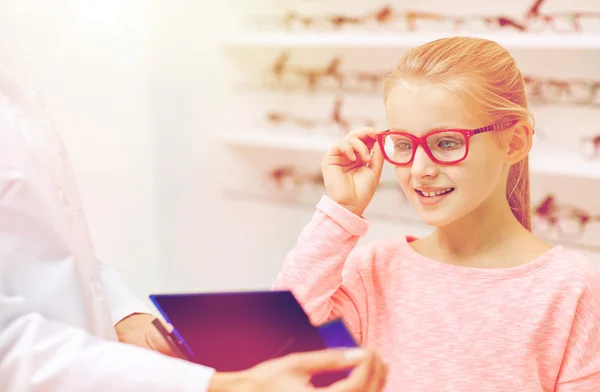 Optician e menina escolhendo óculos na loja de óptica — Fotografia de Stock