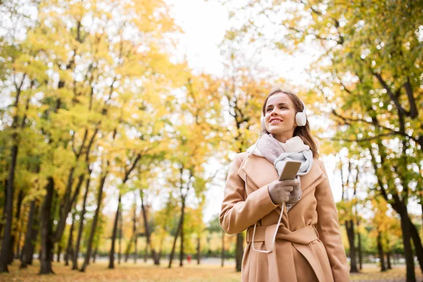 Mulher com smartphone e fones de ouvido no parque de outono — Fotografia de Stock