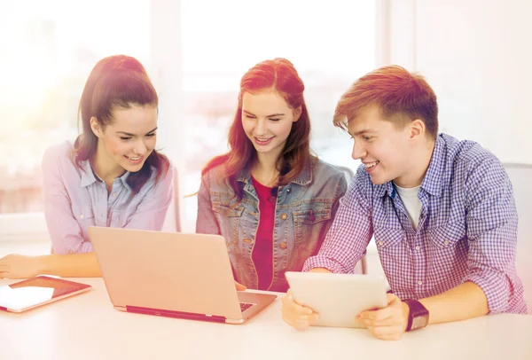 Tres estudiantes sonrientes con ordenador portátil y tableta PC — Foto de Stock