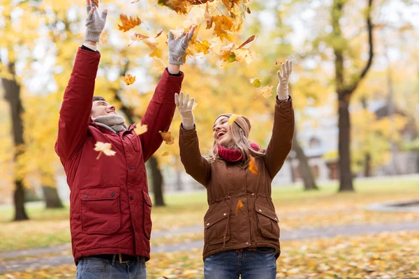 Heureux jeune couple jetant des feuilles d'automne dans le parc — Photo