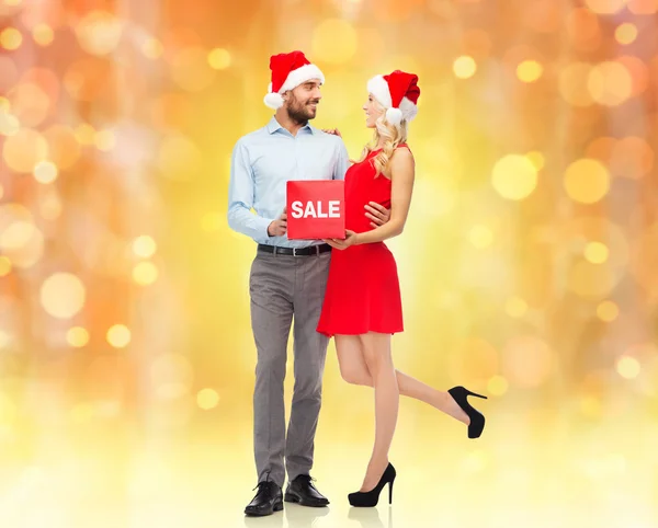Heureux couple dans santa chapeaux avec signe de vente rouge — Photo