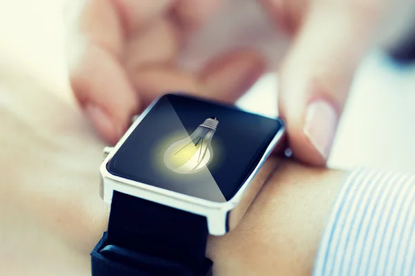 Close up of hands with lightbulb on smartwatch — Stock Photo, Image