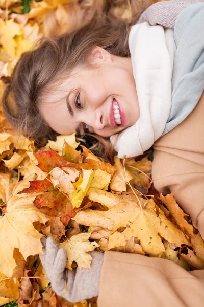 Schöne glückliche Frau, die auf Herbstblättern liegt — Stockfoto