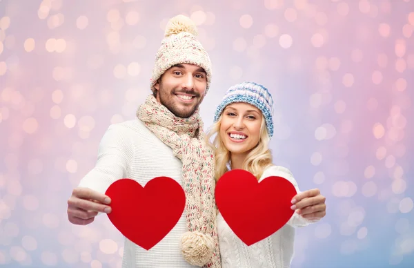 Casal sorridente em roupas de inverno com corações vermelhos — Fotografia de Stock