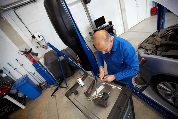 Mechaniker mit Schraubenschlüssel repariert Auto in Werkstatt lizenzfreie Stockfotos