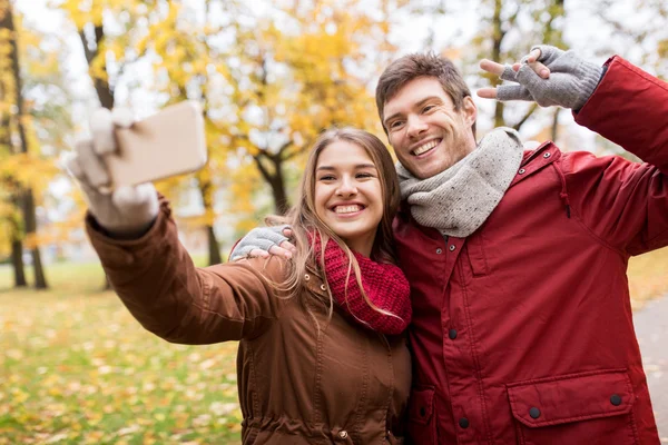 Пара делает селфи на смартфоне в осеннем парке — стоковое фото