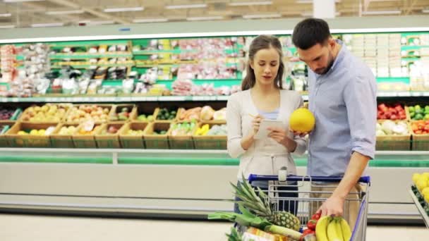 Pareja con comida en el carrito de la compra en la tienda de comestibles — Vídeo de stock