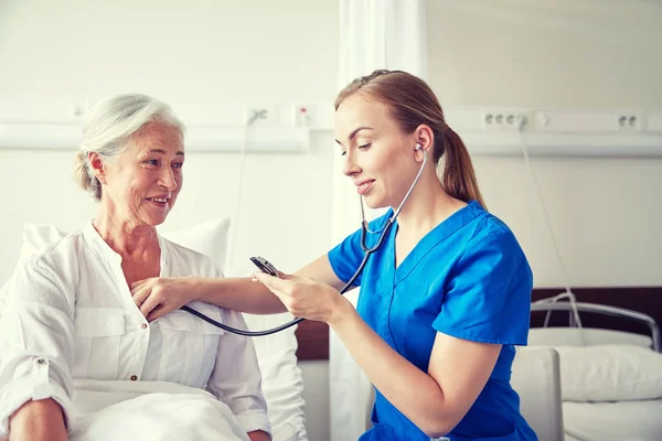 Enfermeira com estetoscópio e mulher idosa na clínica — Fotografia de Stock