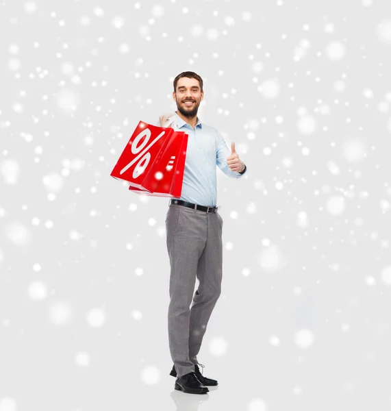 Hombre sonriente con bolsas de compras rojas sobre nieve —  Fotos de Stock