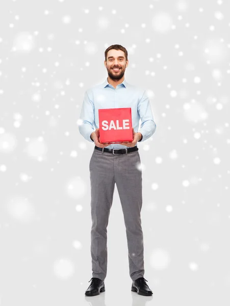 Adam kırmızı satışı işareti ile kar üzerinde gülümseyen — Stok fotoğraf
