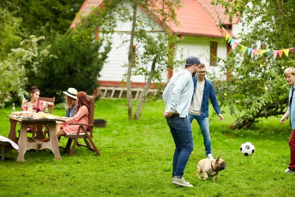 Přáteli, kteří hrají fotbal se psem na letní zahradě — Stock fotografie
