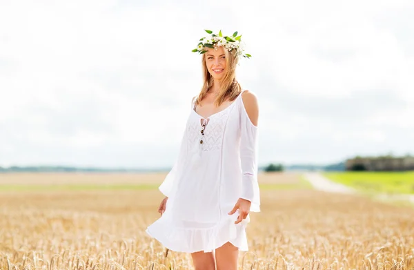 Glückliche junge Frau im Blumenkranz auf einem Getreidefeld — Stockfoto