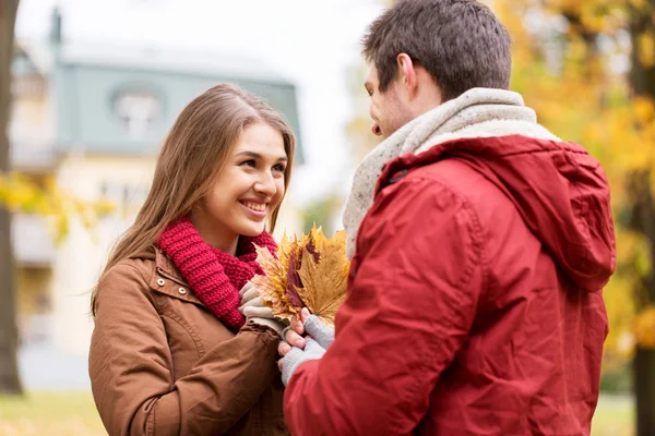 Happy couple with maple leaves in autumn park — Stock Photo, Image