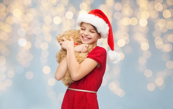 Oyuncak ayı ile santa yardımcı şapkalı kız gülümseyerek — Stok fotoğraf