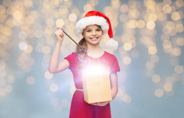 Niña en sombrero de santa con caja de regalo y varita mágica — Foto de Stock