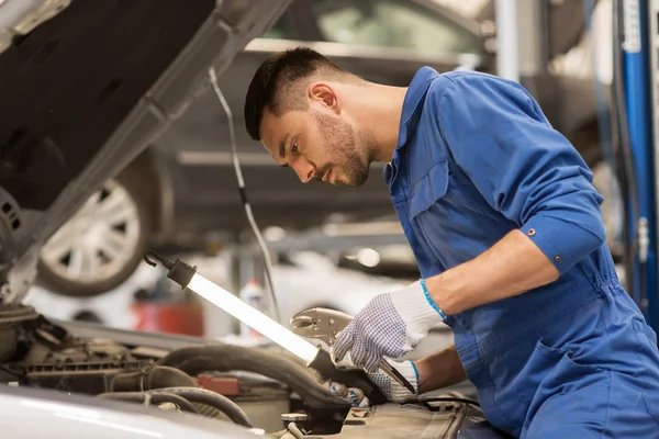 Monteur man met lamp repareren auto bij workshop — Stockfoto