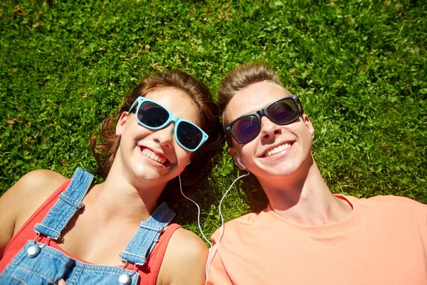 Счастливая пара подростков с наушниками, лежащими на траве — стоковое фото
