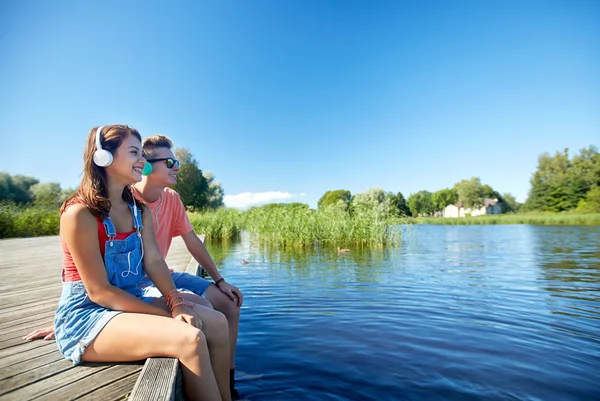 Счастливая пара подростков с наушниками на берегу реки — стоковое фото