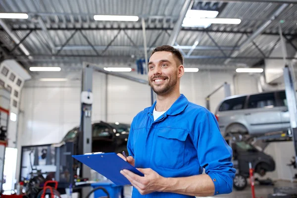 Happy mechanic man with clipboard at car workshop — Stock Photo, Image