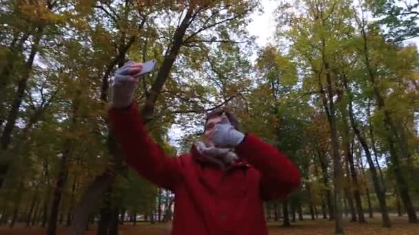 Mann mit Smartphone filmt im Herbstpark — Stockvideo