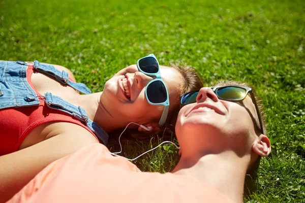 Šťastný dospívající pár s sluchátka ležící na trávě — Stock fotografie