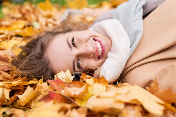 Schöne glückliche Frau, die auf Herbstblättern liegt — Stockfoto