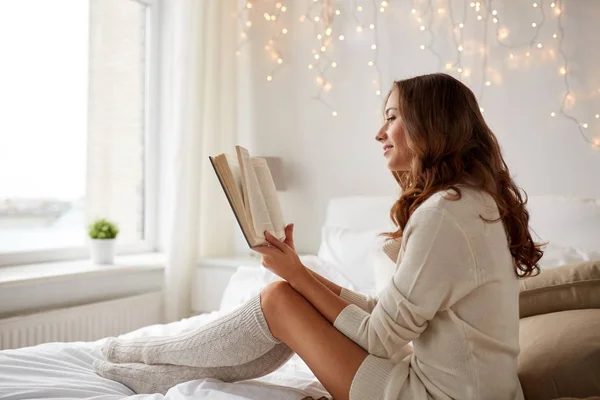 หญิงสาวที่มีความสุขอ่านหนังสือบนเตียงที่บ้าน — ภาพถ่ายสต็อก