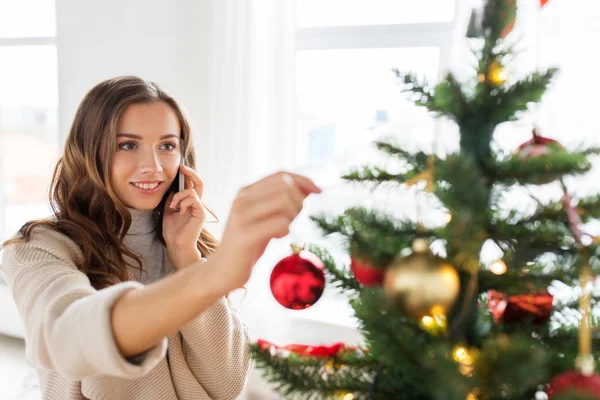 Женщина со смартфоном, украшающая елку — стоковое фото