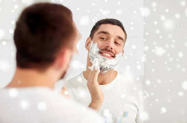 Uomo felice che applica schiuma da barba allo specchio del bagno — Foto Stock