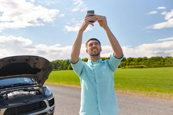 Homem com smartphone e carro quebrado no campo — Fotografia de Stock