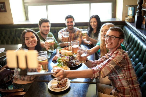 Счастливые друзья с палкой для селфи в баре или пабе — стоковое фото