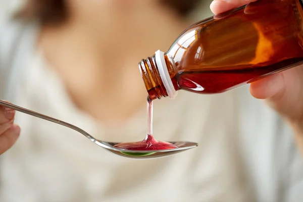 Woman pouring medication from bottle to spoon — Stock Photo, Image