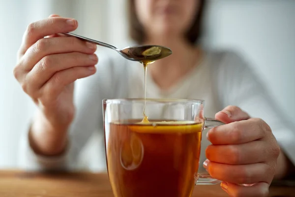 Close up of woman adding honey to tea with lemon — Stock Photo, Image