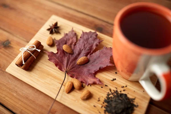 Tazza di tè, foglia d'acero e mandorla su tavola di legno — Foto Stock