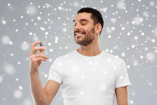 Homem sorridente com perfume masculino sobre fundo de neve — Fotografia de Stock