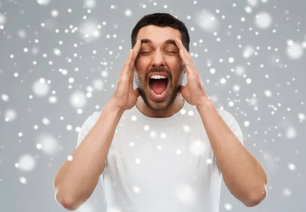 Сумасшедший кричащий мужчина в футболке на фоне снега — стоковое фото