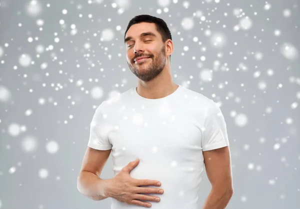 Feliz homem cheio tocando barriga sobre fundo de neve — Fotografia de Stock