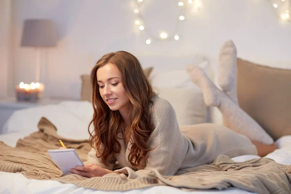 Glad ung kvinna med anteckningsboken i sängen hemma — Stockfoto