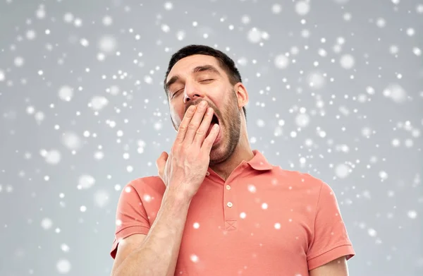 Утомленный зевающий человек на фоне снега — стоковое фото