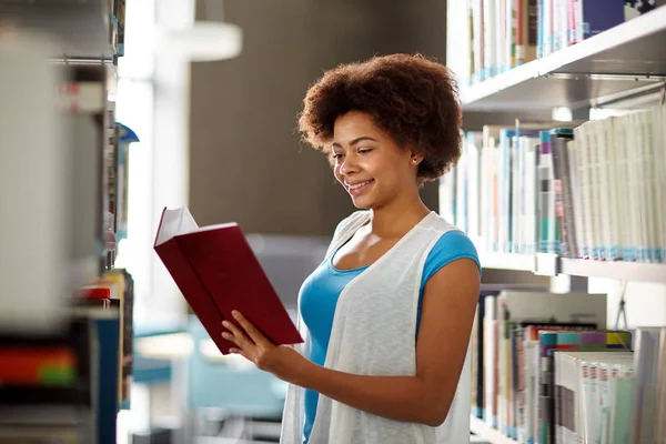 Menina estudante africano feliz ler livro na biblioteca — Fotografia de Stock