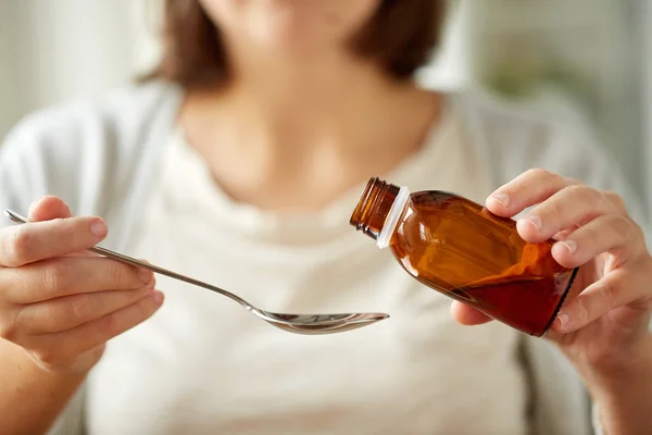 Woman pouring medication from bottle to spoon — Stock Photo, Image