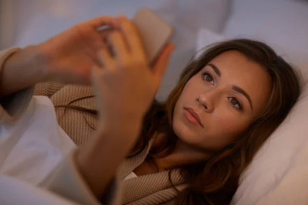 Mujer joven con teléfono inteligente en la cama en el dormitorio en casa — Foto de Stock