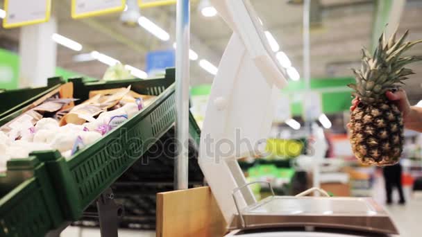 Vrouw met een gewicht van ananas op schaal in supermarkt — Stockvideo