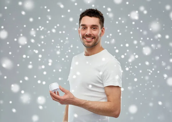 Jovem feliz com frasco de creme sobre a neve — Fotografia de Stock