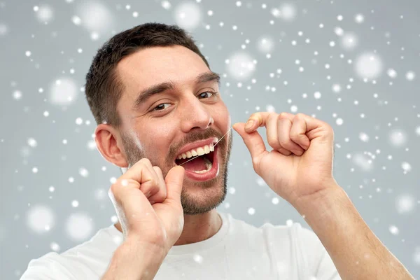 Человек с зубной нитью чистит зубы над снегом — стоковое фото