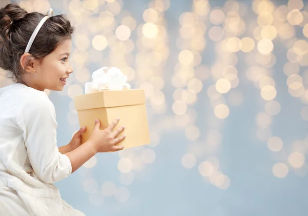 Smiling little girl with gift box over lights — Stock Photo, Image
